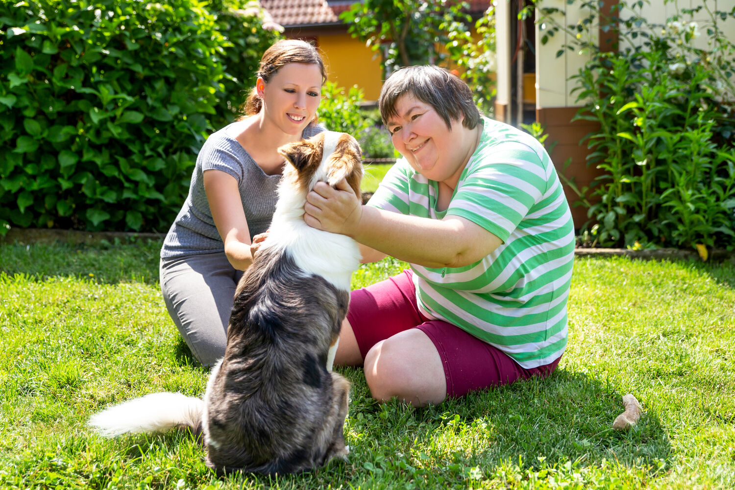 Two women sharing a sunny moment with a dog in the garden